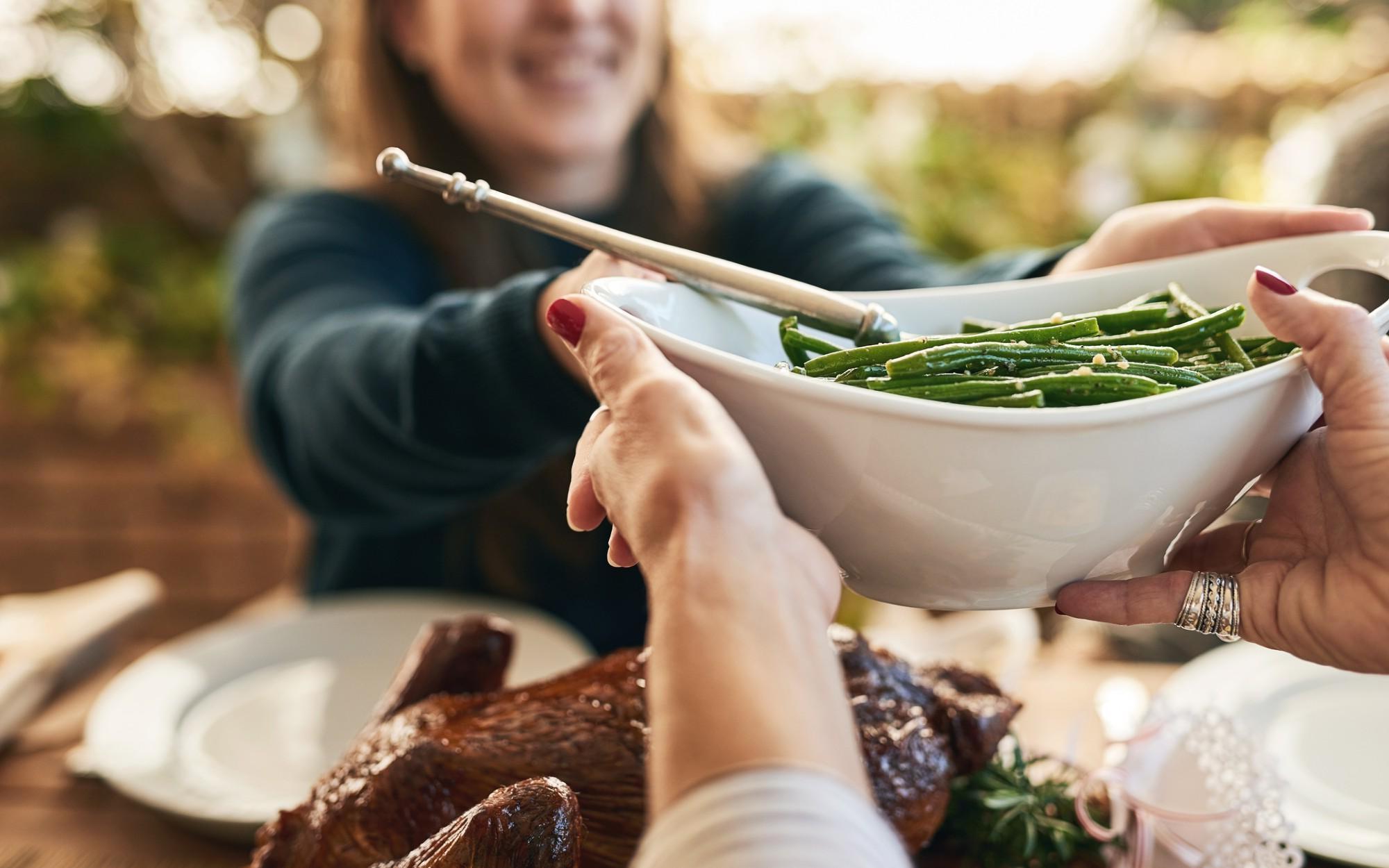 A bowl of bean being passed to another person on a dinner table.