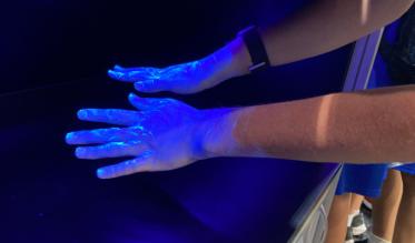 Three children put their hands under UV lights, their backs to the camera.